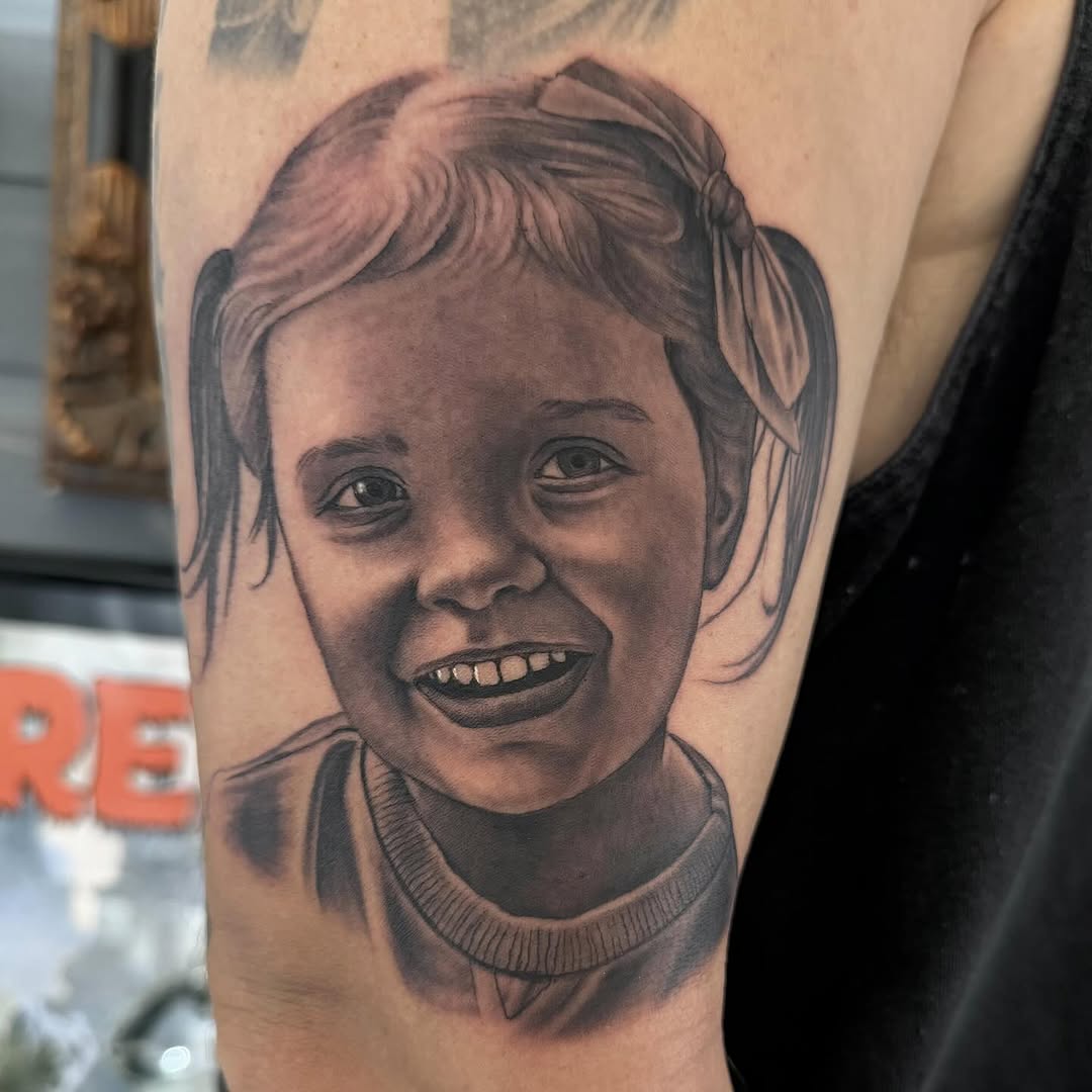 Black-and-grey portrait tattoo of young girl, shoulder