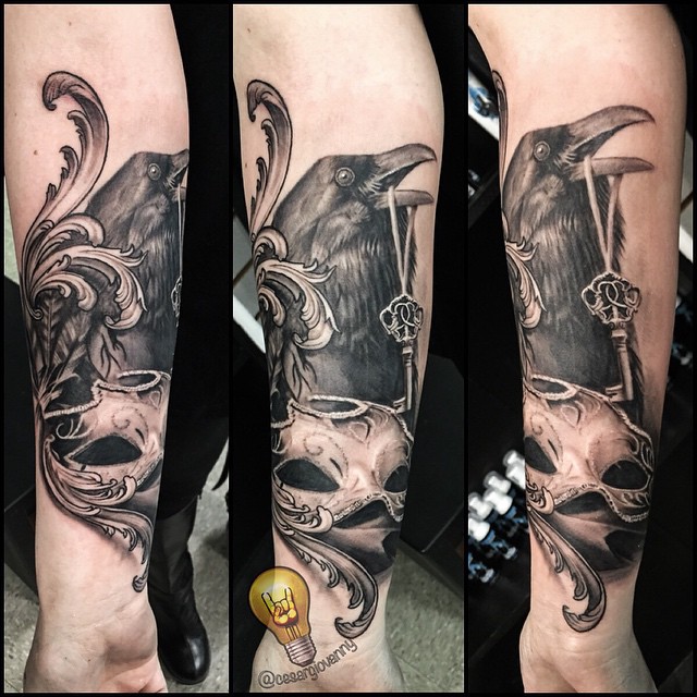 Black-and-grey raven, key & mask forearm tattoo