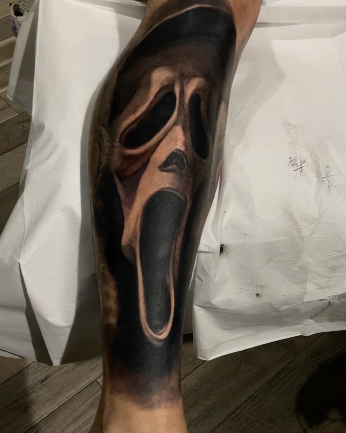 Black-and-grey Scream mask tattoo, calf