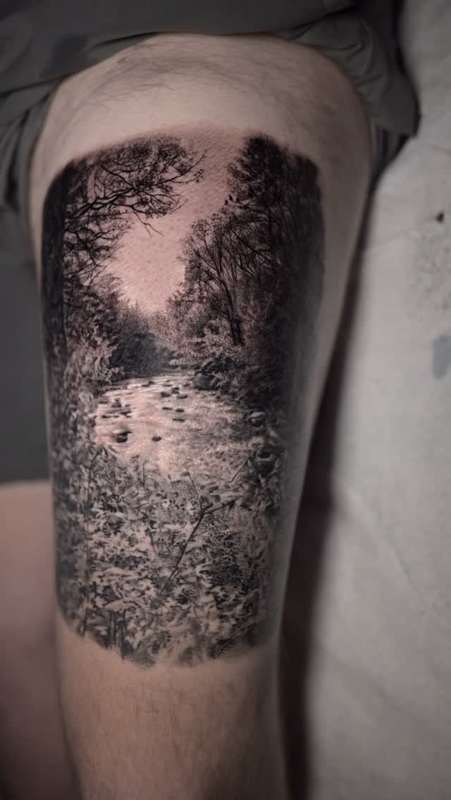 Black-and-grey river landscape tattoo, thigh