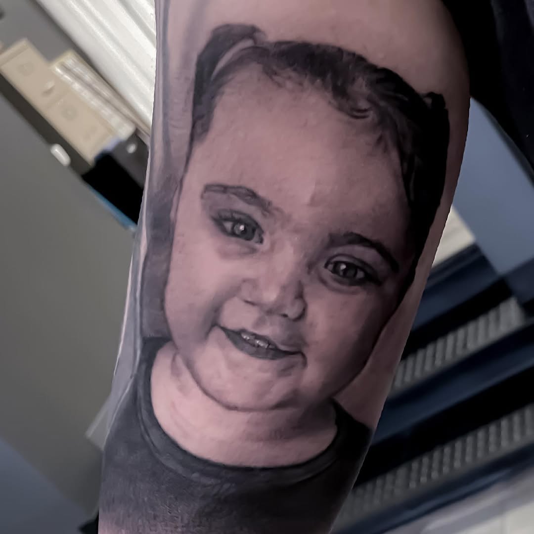 Black-and-grey child portrait tattoo, arm
