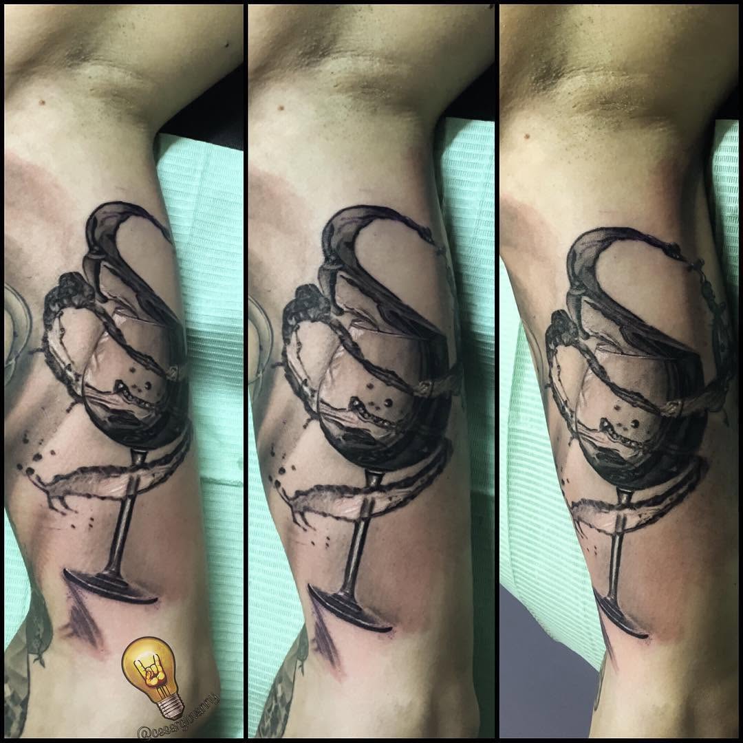 Black-and-grey wine glass tattoo on bicep