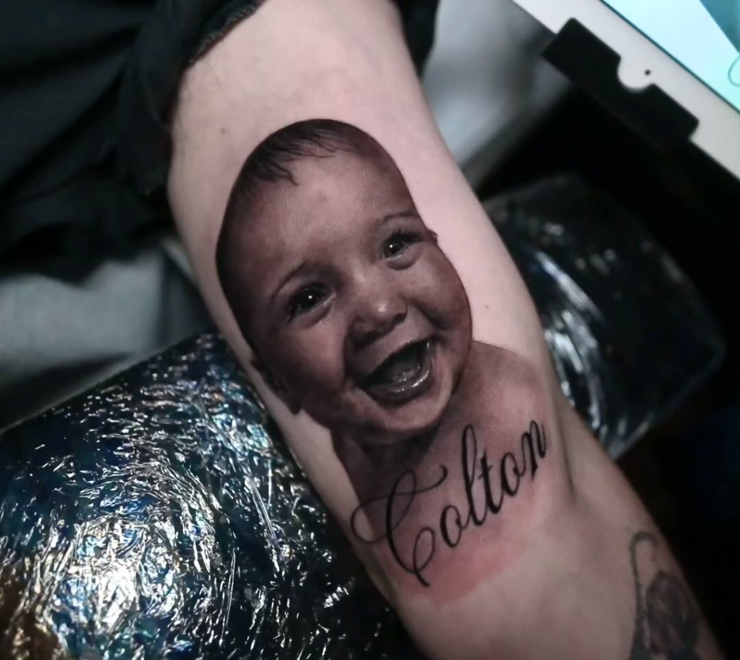 Black-and-grey baby portrait tattoo with name