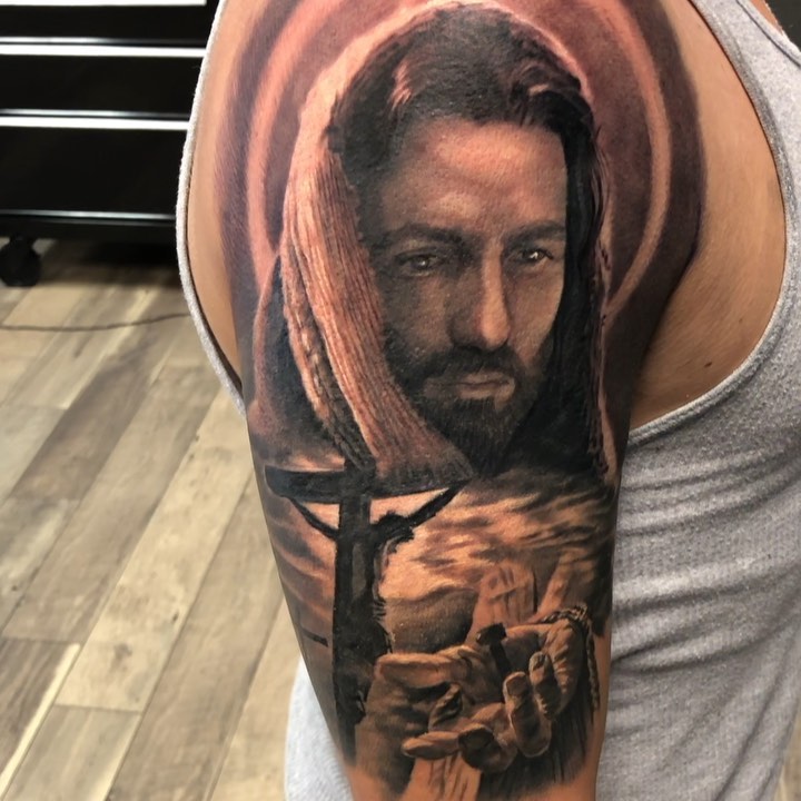 Black-and-grey Jesus portrait tattoo, bicep