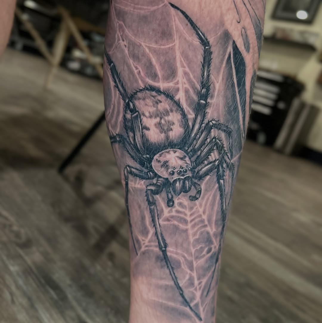 Realistic spider and web leg tattoo in black-and-grey