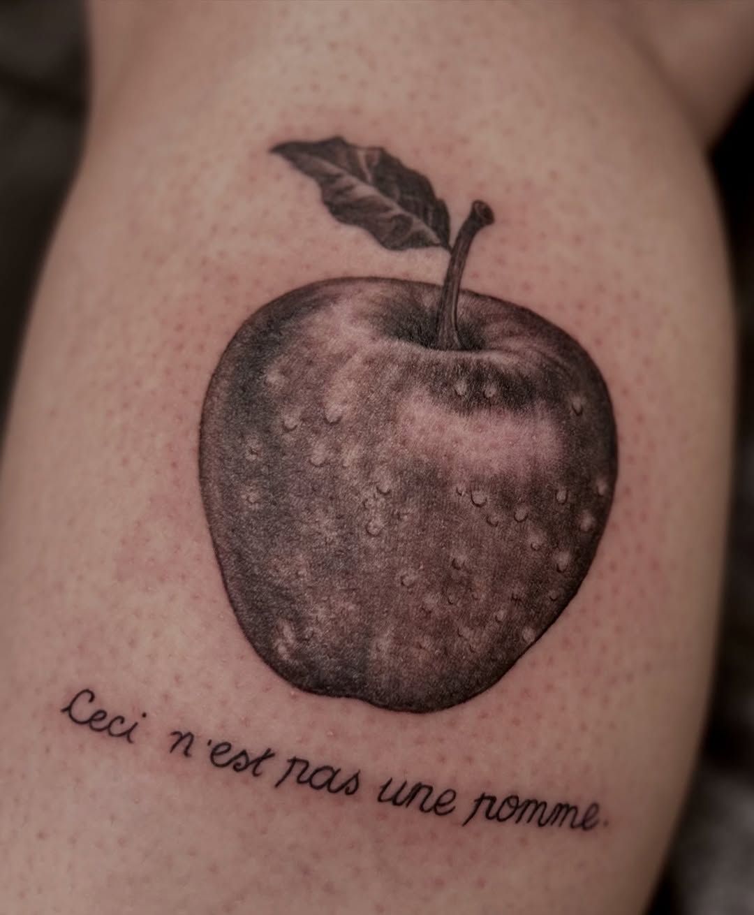 Realistic apple with leaf and French script tattoo
