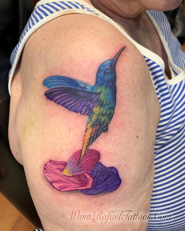 Realistic hummingbird with flower petals tattoo on aged skin