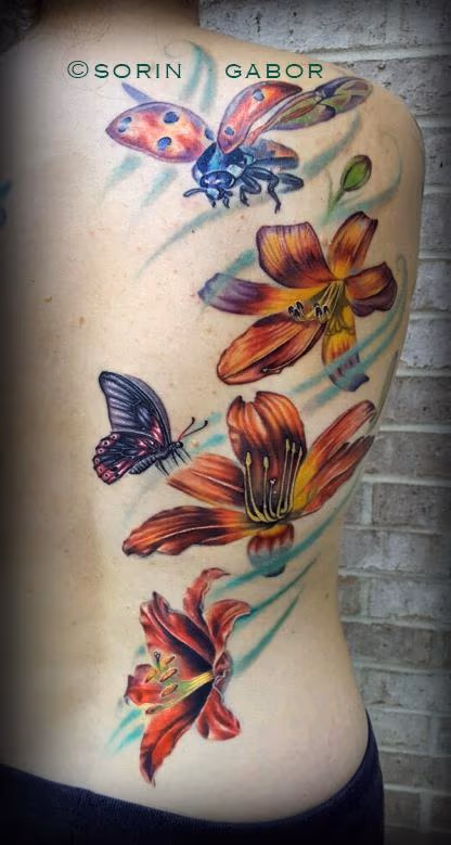 Realistic lilies, lady bug, and butterly half back feminine tattoo