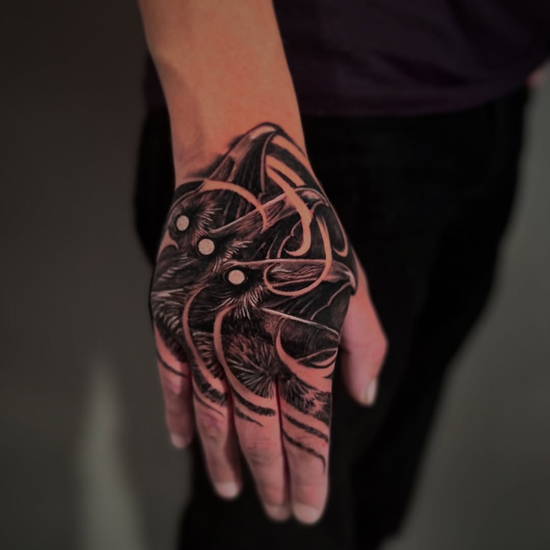 Black-and-grey raven hand tattoo with ornaments