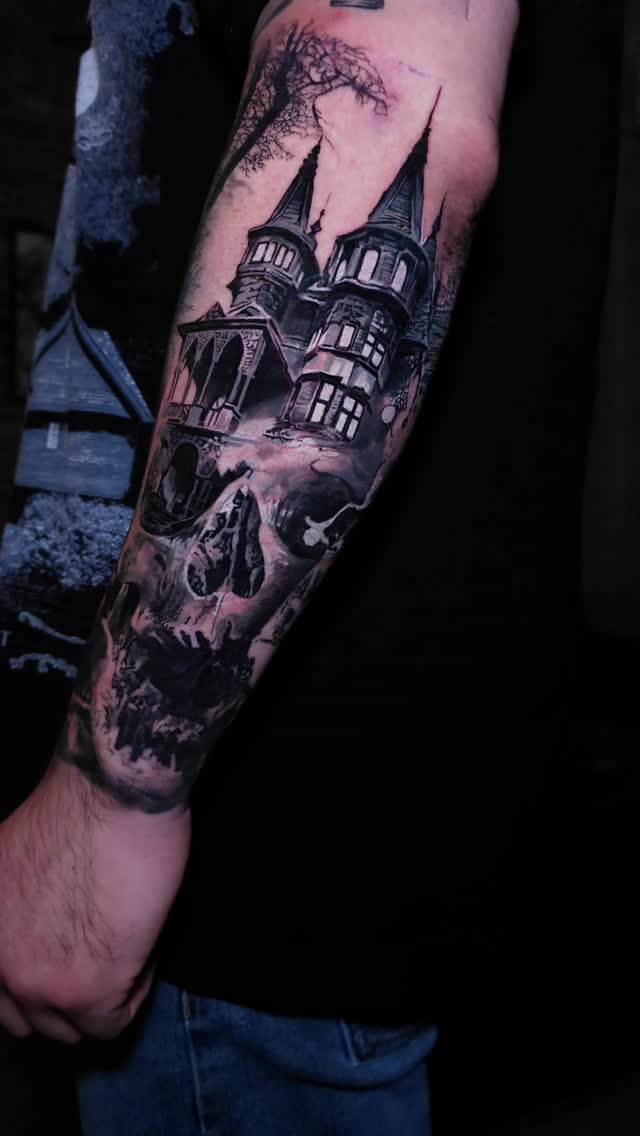Haunted mansion with skull forearm tattoo, black-and-grey